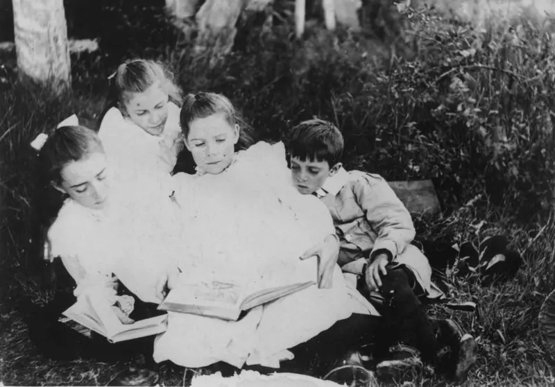 Four children sharing books on the grass, Queensland, around 1905